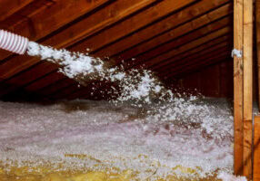 Worker Spraying mineral rock wool of thermal insulation layer under the roof house attic insulation